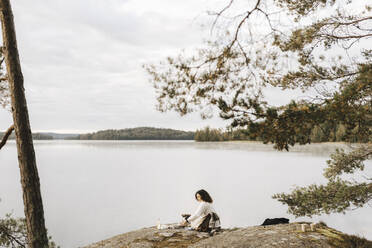 Young woman sitting on rock at lakeshore - MASF27233