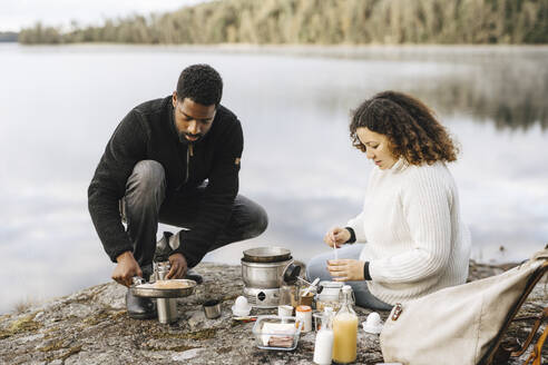Couple preparing food at lakeshore while camping - MASF27235