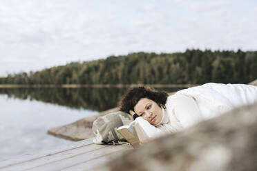 Eine Frau liest ein Buch auf einem Steg über dem See - MASF27242