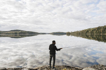 Full length rear view of man fishing in lake with reflection of clouds - MASF27276