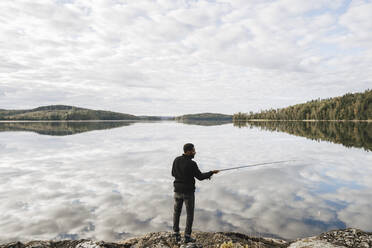 Rückansicht eines Mannes beim Fischen im See mit Wolkenreflexion in voller Länge - MASF27276