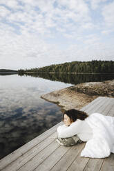 Young woman admiring lake while lying on pier - MASF27278