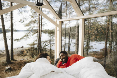 Happy couple talking while lying in cottage during weekend - MASF27282