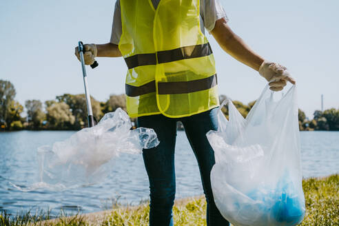 Mittelteil eines jungen männlichen Umweltschützers, der am See Plastik aufhebt - MASF27295