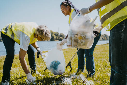 Männliche und weibliche Freiwillige reinigen an einem sonnigen Tag Plastik am Seeufer - MASF27298