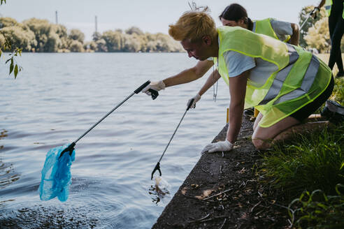 Männliche und weibliche Umweltschützer sammeln mit ihren Klauen Plastik aus dem See auf - MASF27302