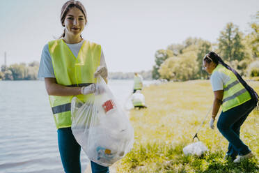 Porträt einer lächelnden Frau mit Plastiktüte am Seeufer - MASF27306