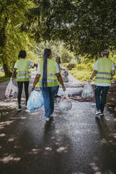 Multiracial female volunteers walking with plastics in park - MASF27318