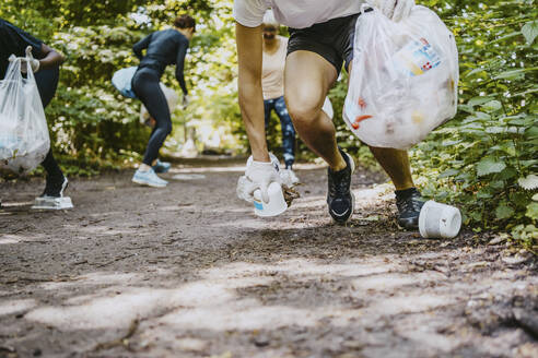 Männliche und weibliche Umweltschützer, die beim Joggen im Park Plastik aufheben - MASF27325