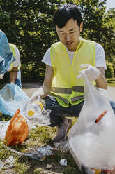 Young male volunteer picking up plastics at park - MASF27330