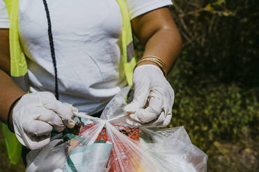 Mittelteil einer Umweltschützerin, die im Park einen Knoten in eine Plastiktüte macht - MASF27340