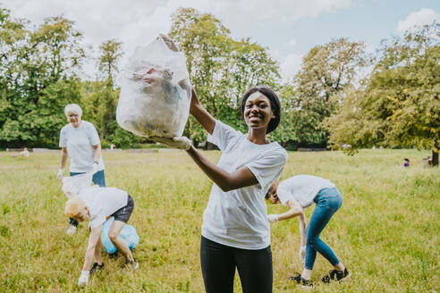 Porträt einer Umweltschützerin, die Plastikmüll zeigt, während Freiwillige im Park putzen - MASF27342