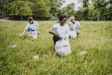 Lächelnde männliche und weibliche Freiwillige, die Plastik im Park aufsammeln - MASF27344