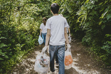 Rear view of male and female environmentalists walking with plastic bags in park - MASF27368