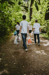 Rear view of female and male volunteers with plastic waste walking in park - MASF27369