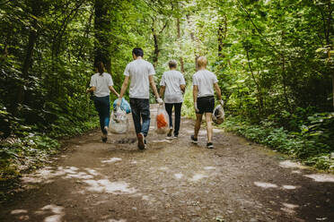 Female and male volunteers walking with plastic waste in park - MASF27370