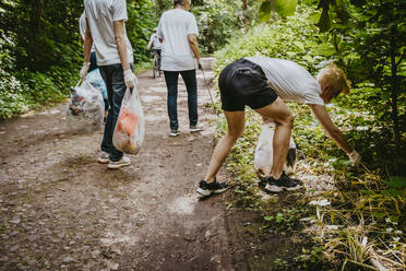 Young man picking up garbage while volunteering with environmentalists at park - MASF27371