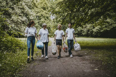 Female and male volunteers talking while walking with plastic bags in park - MASF27373