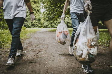 Niedriger Ausschnitt von männlichen und weiblichen Freiwilligen mit Plastiktüten im Park - MASF27374