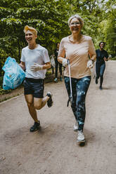 Fröhliche Frau und Mann beim Joggen mit Plastiktüte im Park - MASF27384
