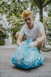 Männlicher Umweltschützer, der eine Plastiktüte auf dem Gehweg festbindet - MASF27392