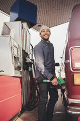 Lächelnder Mann beim Tanken eines Campingbusses an einer Tankstelle - MASF27396