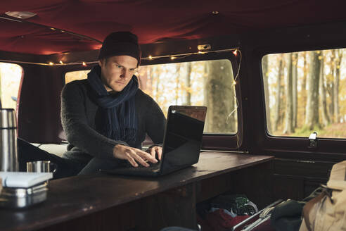 Male freelancer working on laptop in camping van - MASF27425