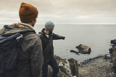 Man pointing at rock in sea to male friend during vacation - MASF27434