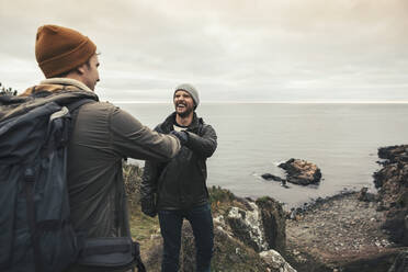 Happy male friends doing fist bump against sea - MASF27435