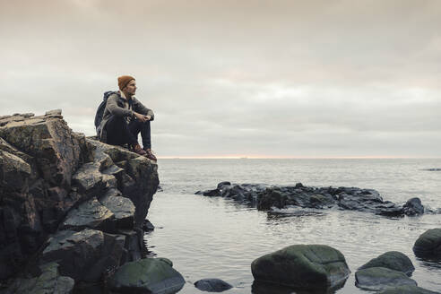 Nachdenklicher Mann, der auf einem Felsen am Meer sitzt - MASF27439