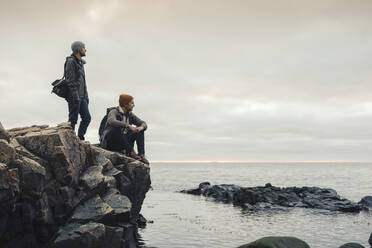 Male friends on rocks at beach during sunset - MASF27440