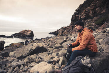 Nachdenklicher Mann sitzt auf einem Felsen am Strand - MASF27446