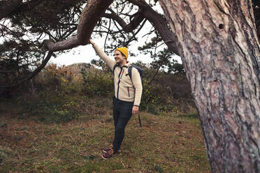 Smiling man holding tree branch while standing in forest - MASF27452