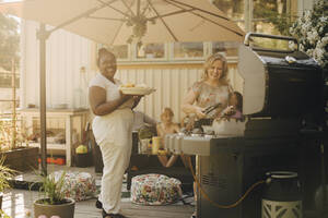Lächelnde Frauen bei der Zubereitung von Speisen auf einem Grill im Innenhof - MASF27475
