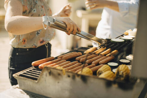 Mittelteil einer Frau bei der Zubereitung von Speisen auf einem Grill während einer Gartenparty - MASF27494