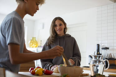 Smiling girl looking at brother preparing food in kitchen - MASF27498