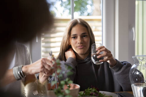 Mädchen hält ein Trinkglas, während sie mit ihrer Mutter zu Hause isst - MASF27510