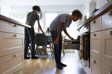 Boy searching in drawer while family at dining table - MASF27515