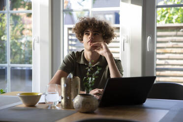 Jugendlicher, der zu Hause mit seinem Laptop sitzt und nachdenkt - MASF27518