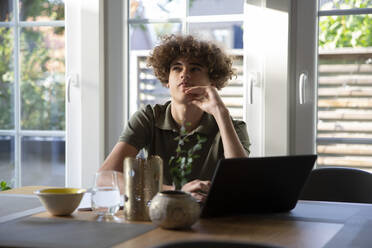 Teenage boy contemplating while sitting with laptop at home - MASF27518