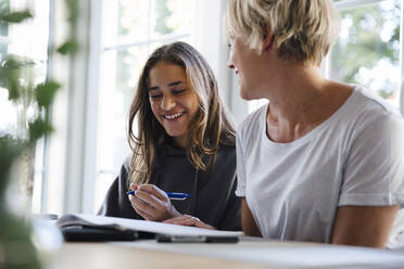 Mother and daughter laughing while studying at home - MASF27538