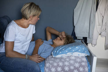Blonde Frau im Gespräch mit ihrem Sohn, der zu Hause auf dem Bett liegt - MASF27550