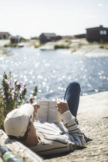 Mann liest ein Buch, während er an einem sonnigen Tag auf einem Felsen liegt - MASF27584