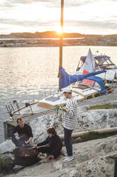 Männliche und weibliche Freunde bereiten bei Sonnenuntergang am Meer Essen zu - MASF27605