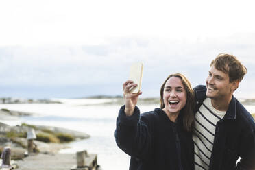 Happy heterosexual couple taking selfie through smart phone during vacation - MASF27628