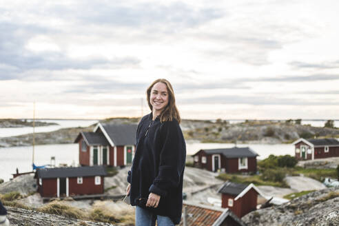 Happy woman looking away against cottages during vacation - MASF27633