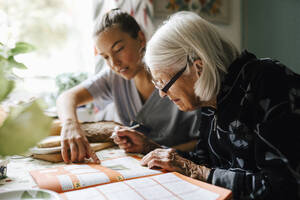 Eine Krankenschwester löst ein Kreuzworträtsel mit einer älteren Frau, während sie zu Hause in der Küche sitzt - MASF27648