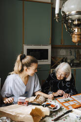 Lächelnde Krankenschwester unterrichtet ältere Frau am Esstisch in der Küche - MASF27652