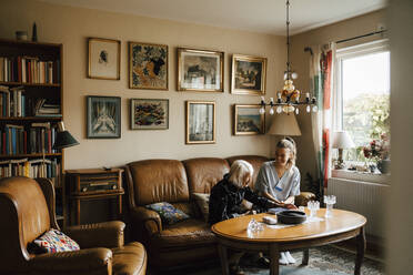 Weibliche Krankenschwester und ältere Frau unterhalten sich auf dem Sofa im Wohnzimmer sitzend - MASF27659