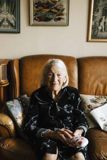 Portrait of senior woman sitting on sofa in living room - MASF27671